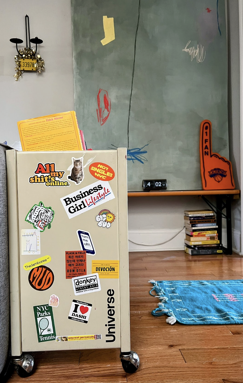 A sticker-covered rolling cabinet in front of a painted wall and stacked books