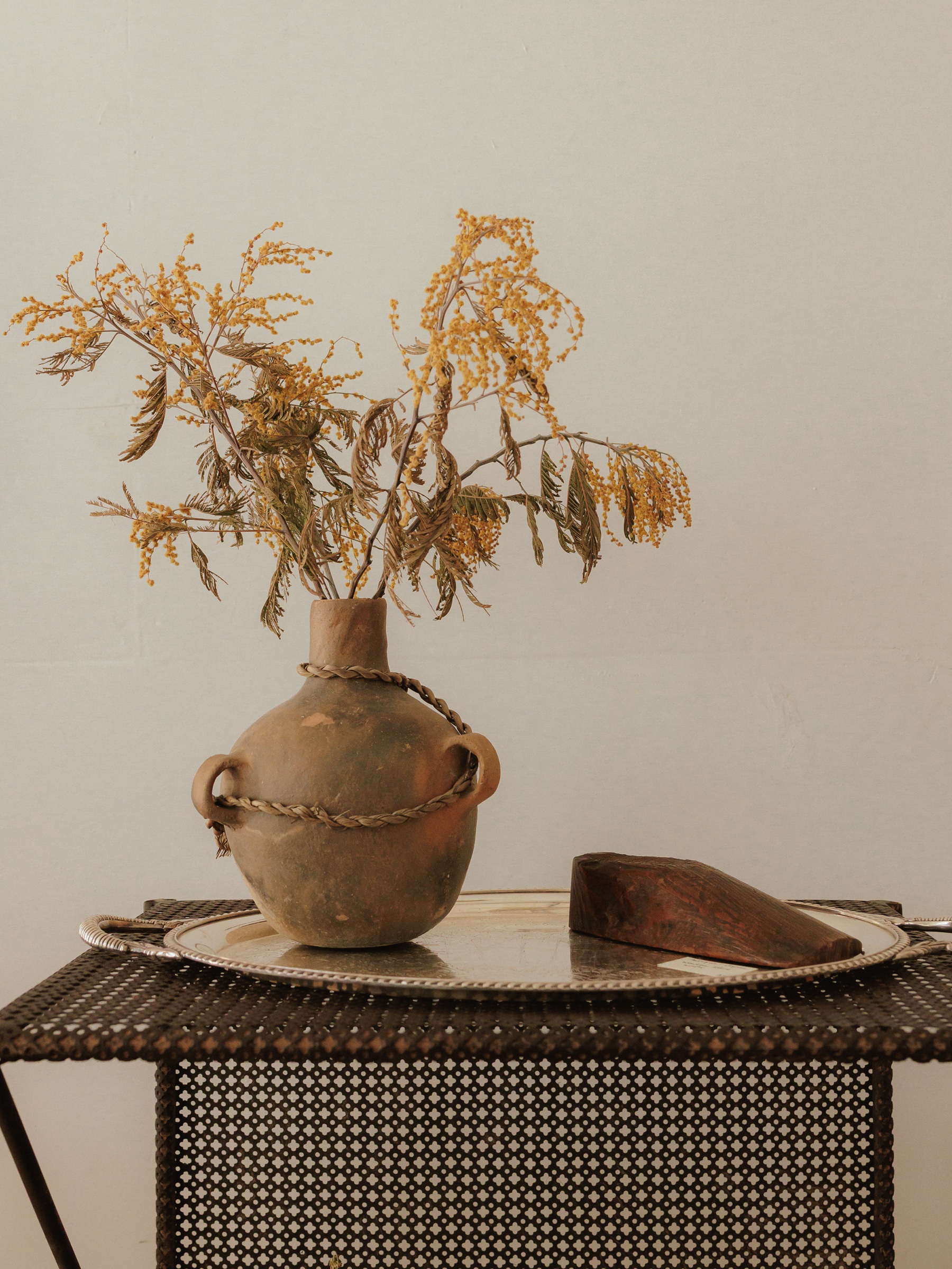 Dried flowers in a clay vessel beside a wooden foot form