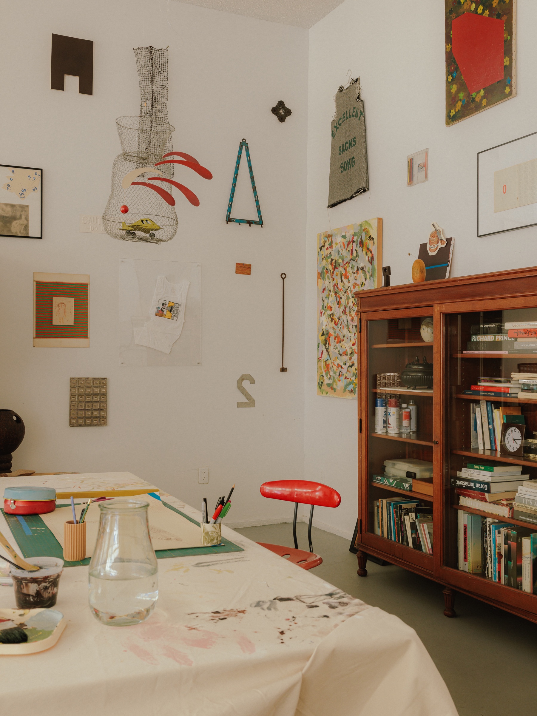 An artist's desk, a red chair, and a wall of collected artwork