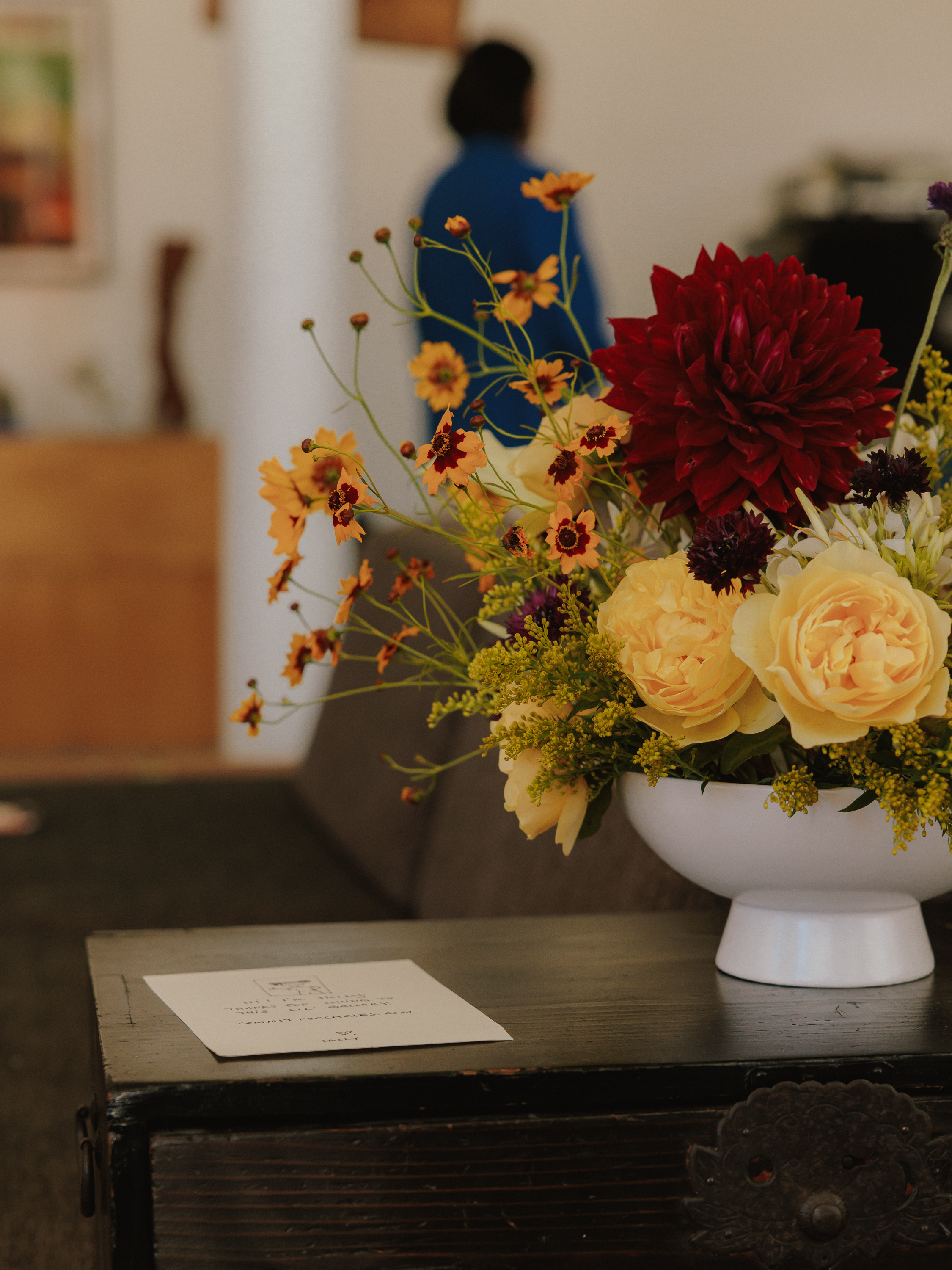 A colorful flower arrangement in a white vessel on a dark wooden table