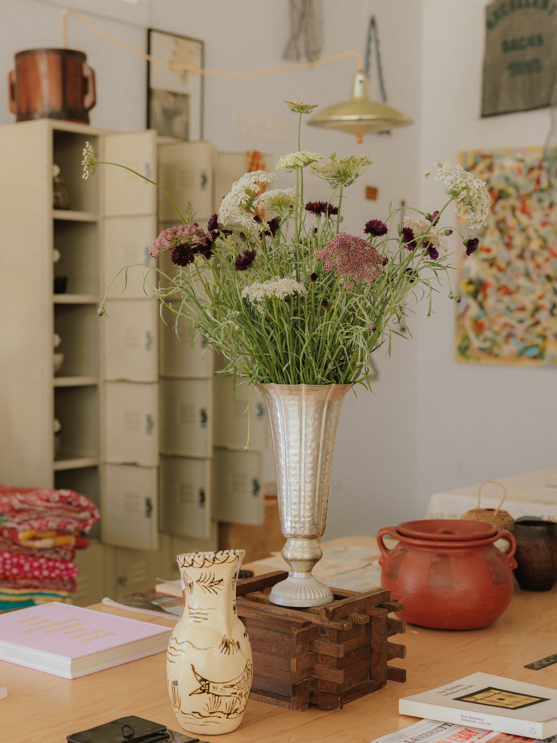 Flowers in a silver vase with handmade vessels arranged in a studio