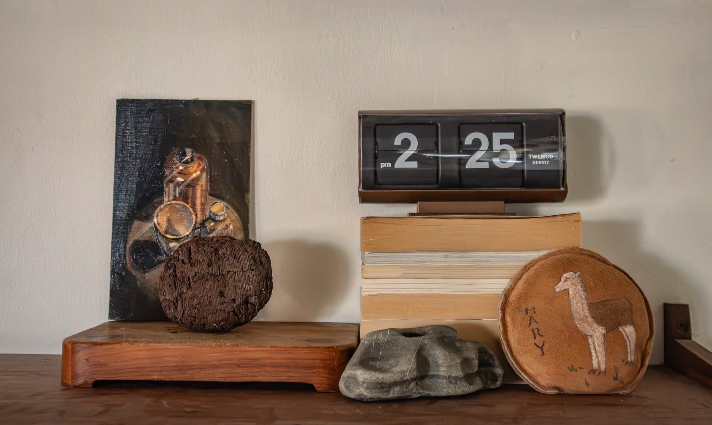 A flip clock, books, stones, and artwork arranged on a shelf