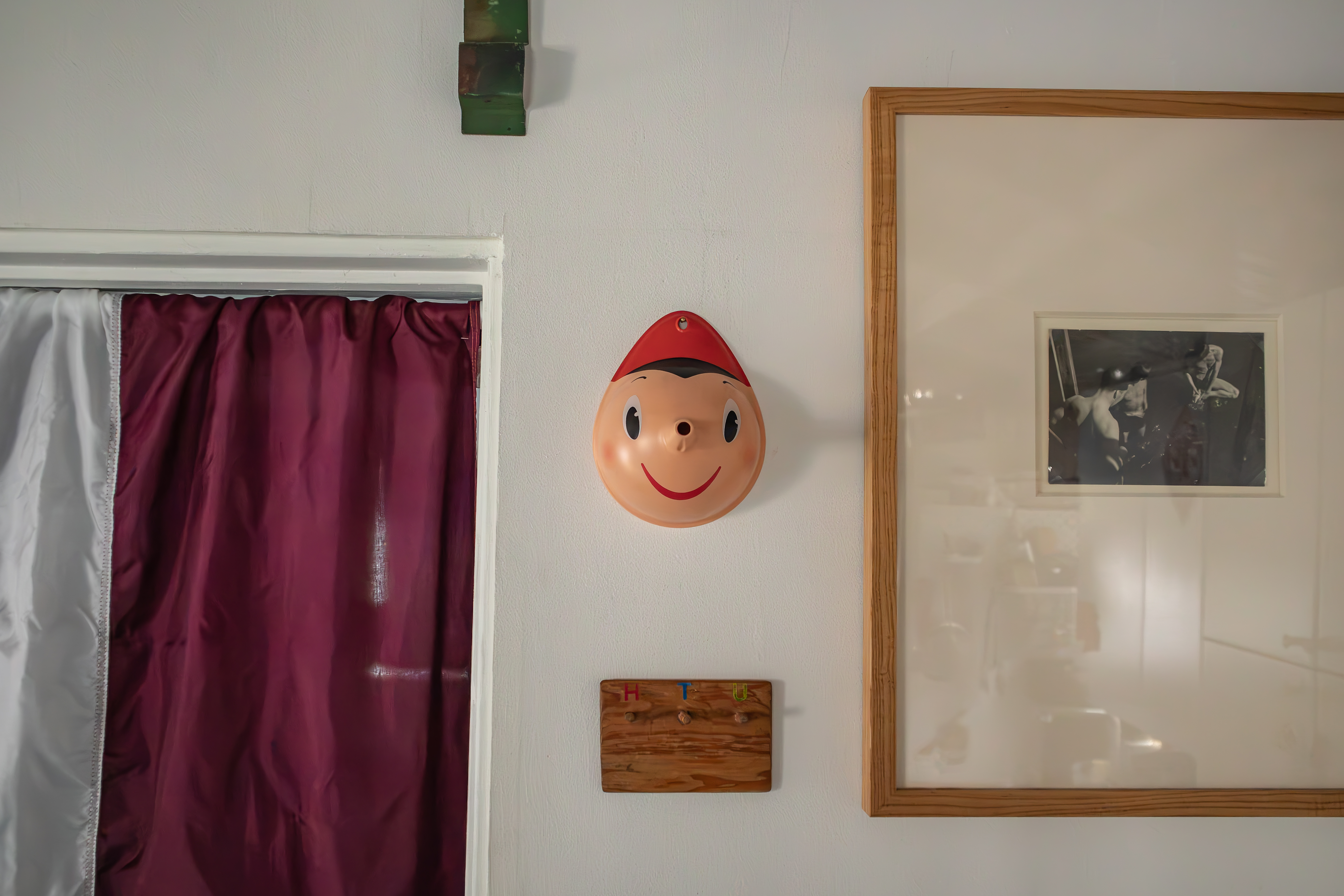 A red smiling face mask and framed artwork on a wall