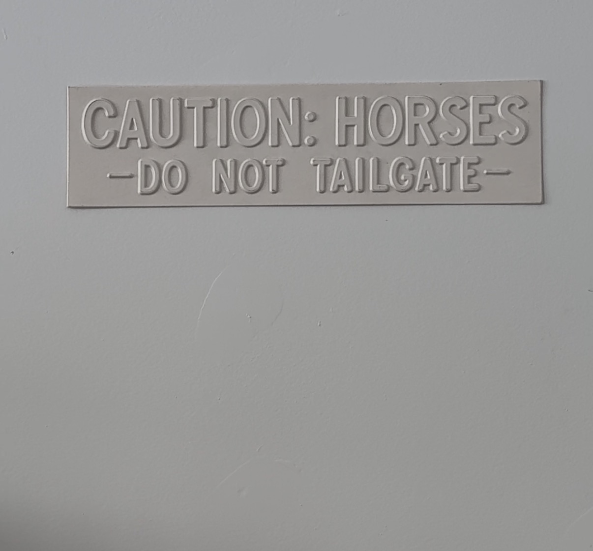 A white Caution: Horses — Do Not Tailgate sign displayed on a wall