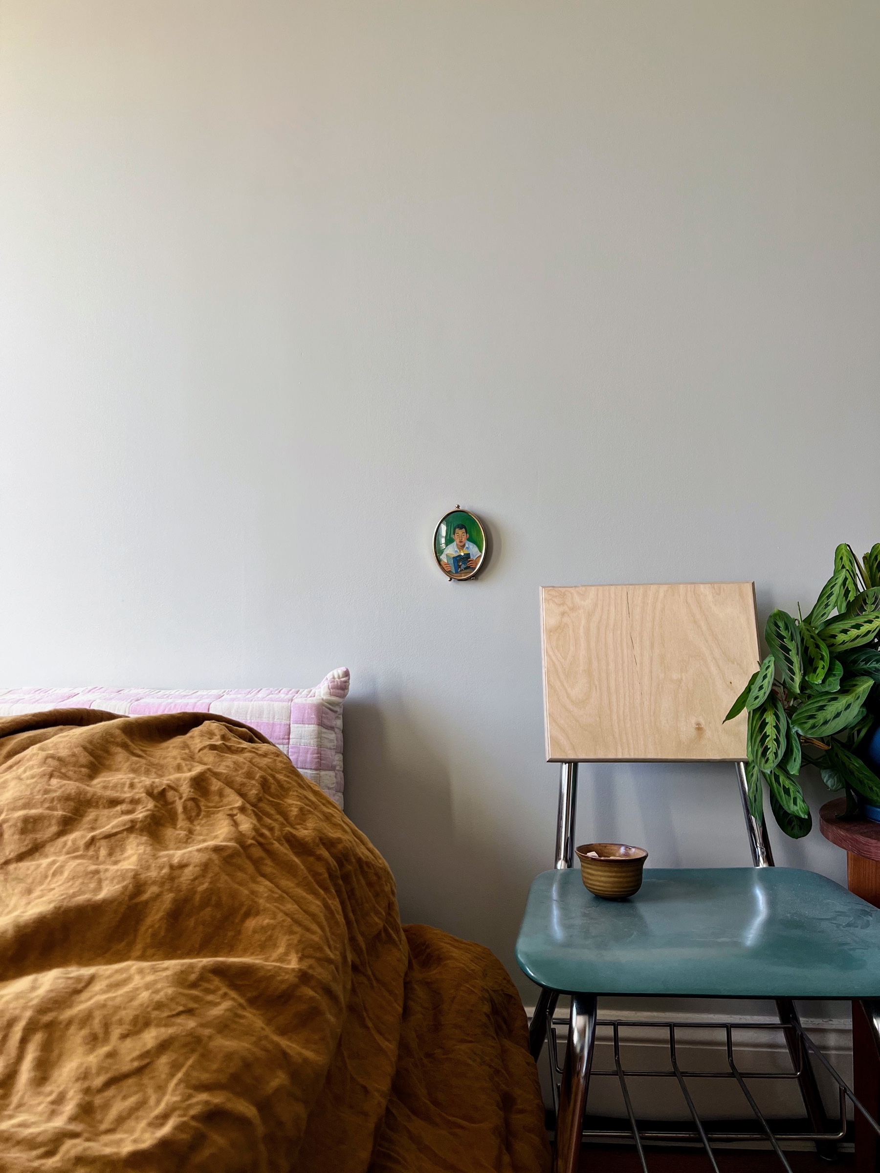 Bed, chair, artwork, and plants against a pale wall