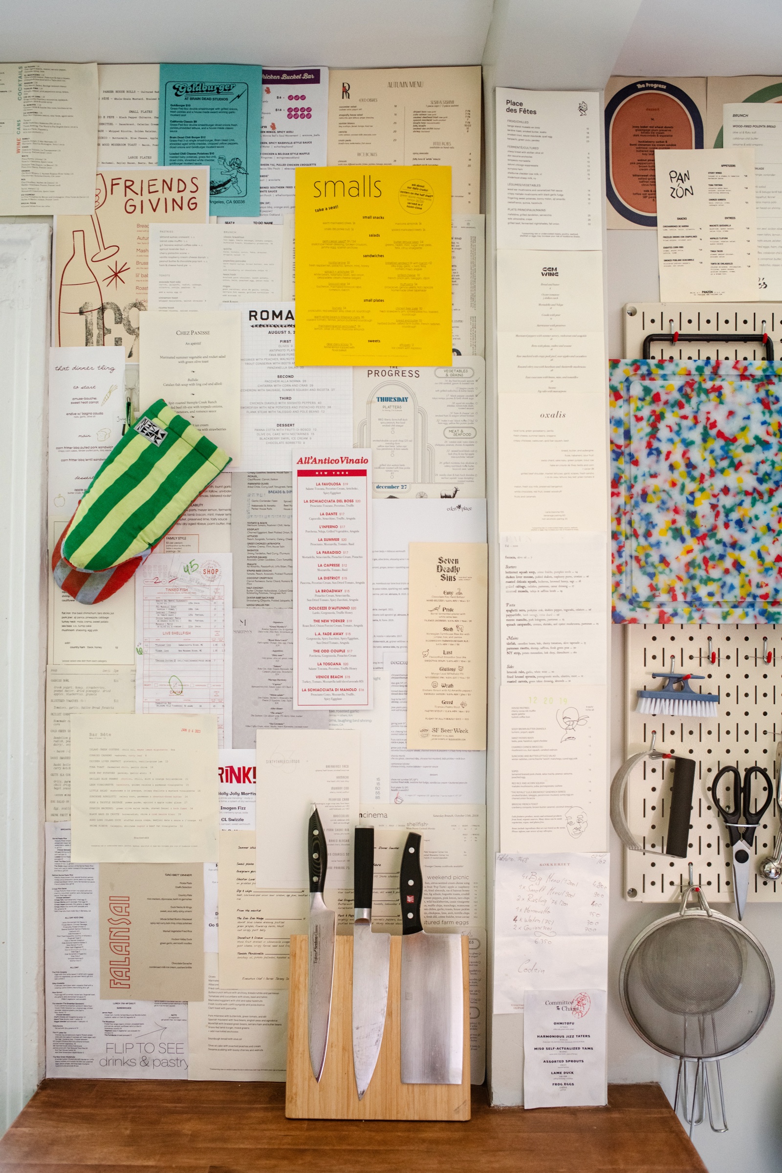 A wall covered with collected menus beside a kitchen tool board