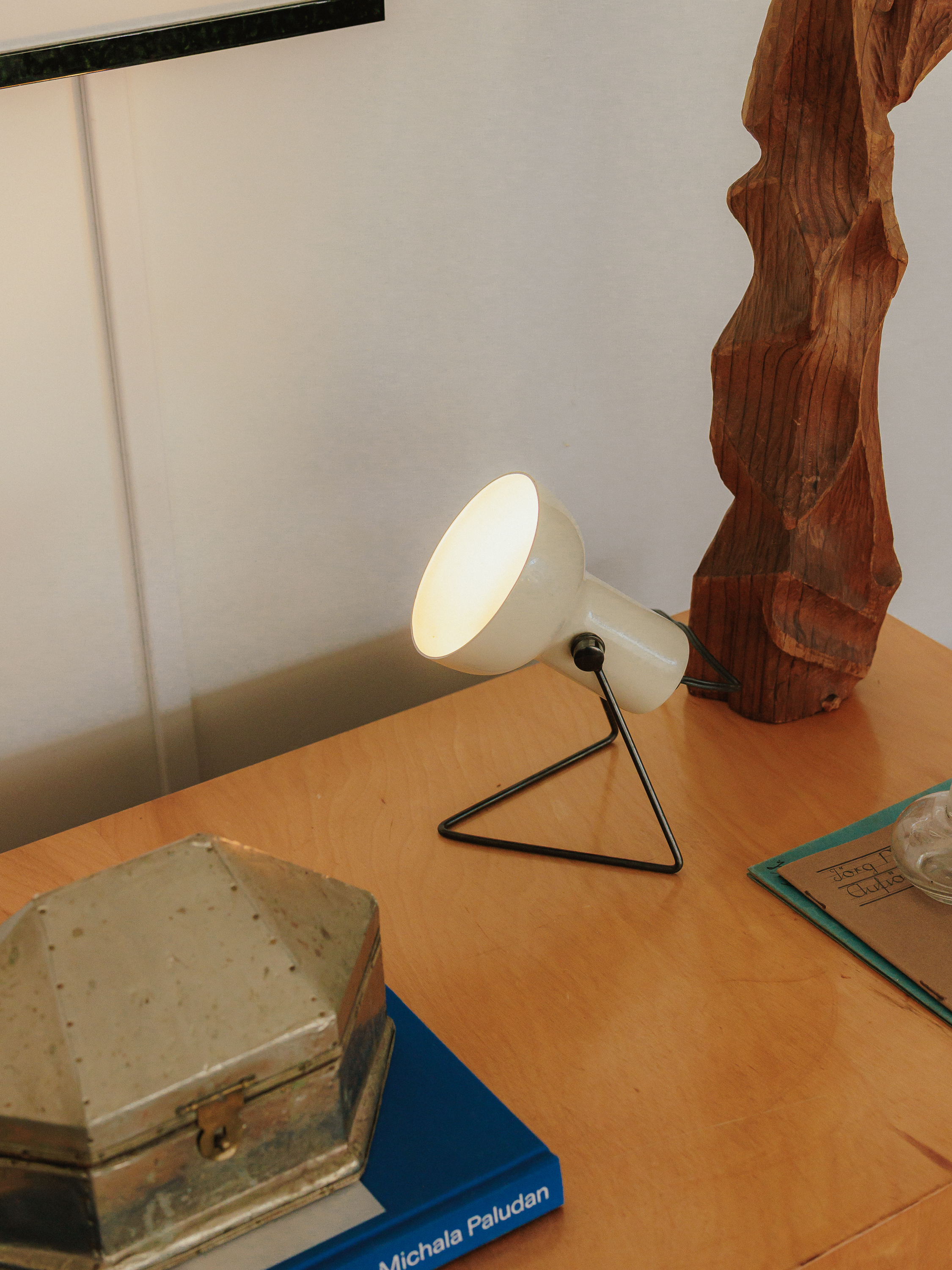 A white desk lamp beside a carved wooden sculpture and collected objects